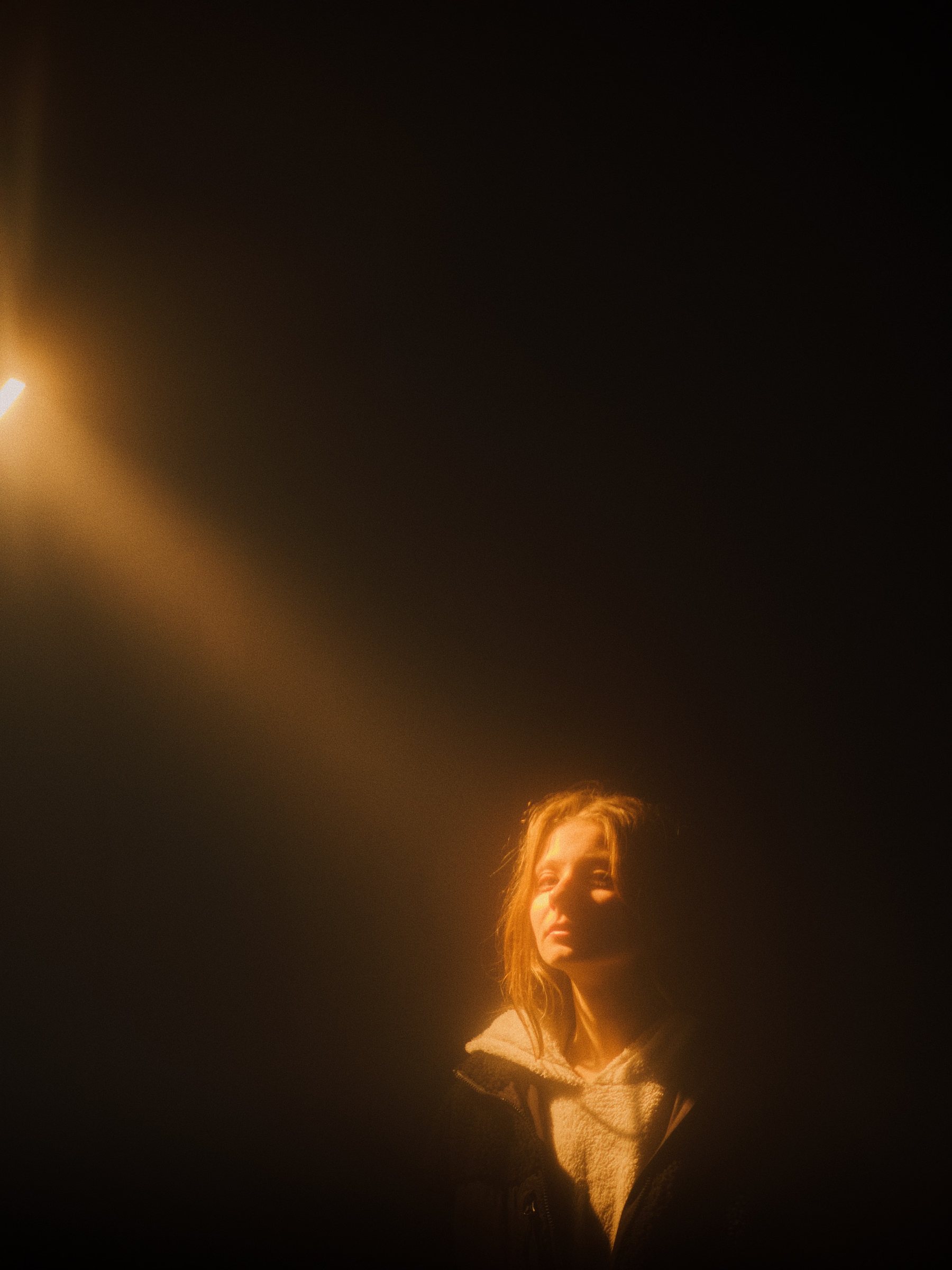 A figure lit by a single warm beam of light in a dark room