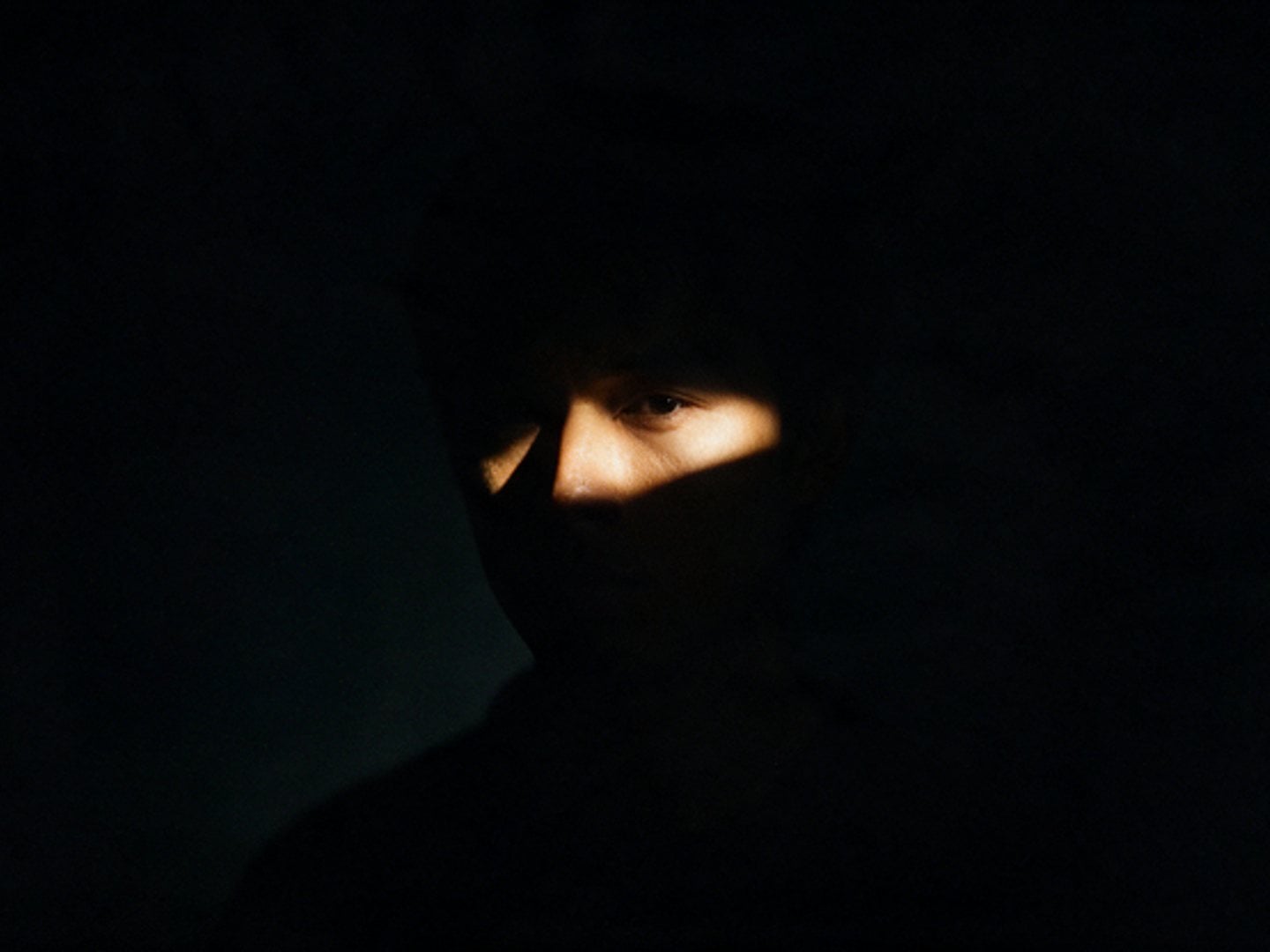 A face half-lit by a narrow blade of warm light in darkness