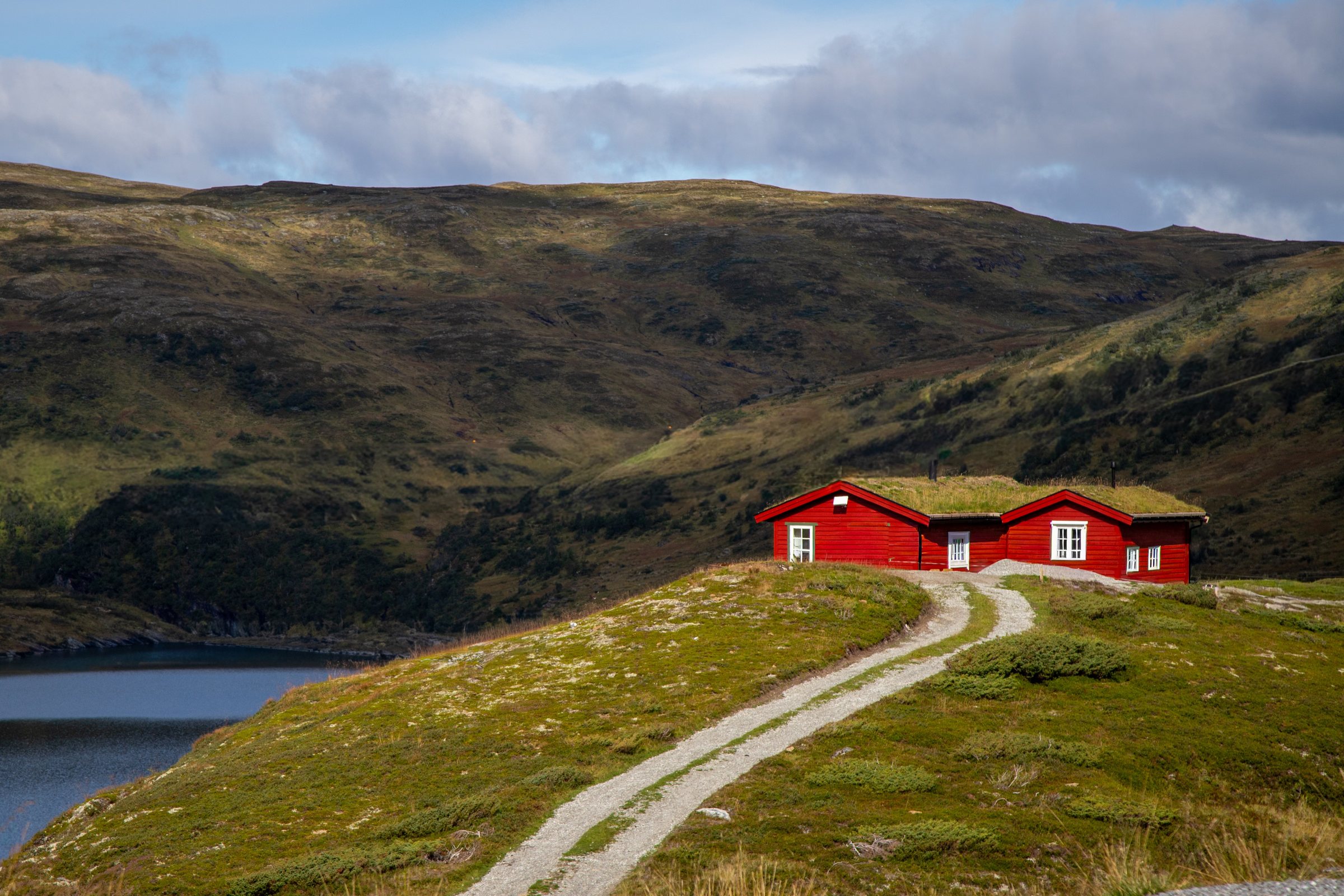 Red turf-roofed cabins on a ridge above a mountain lake in Norway