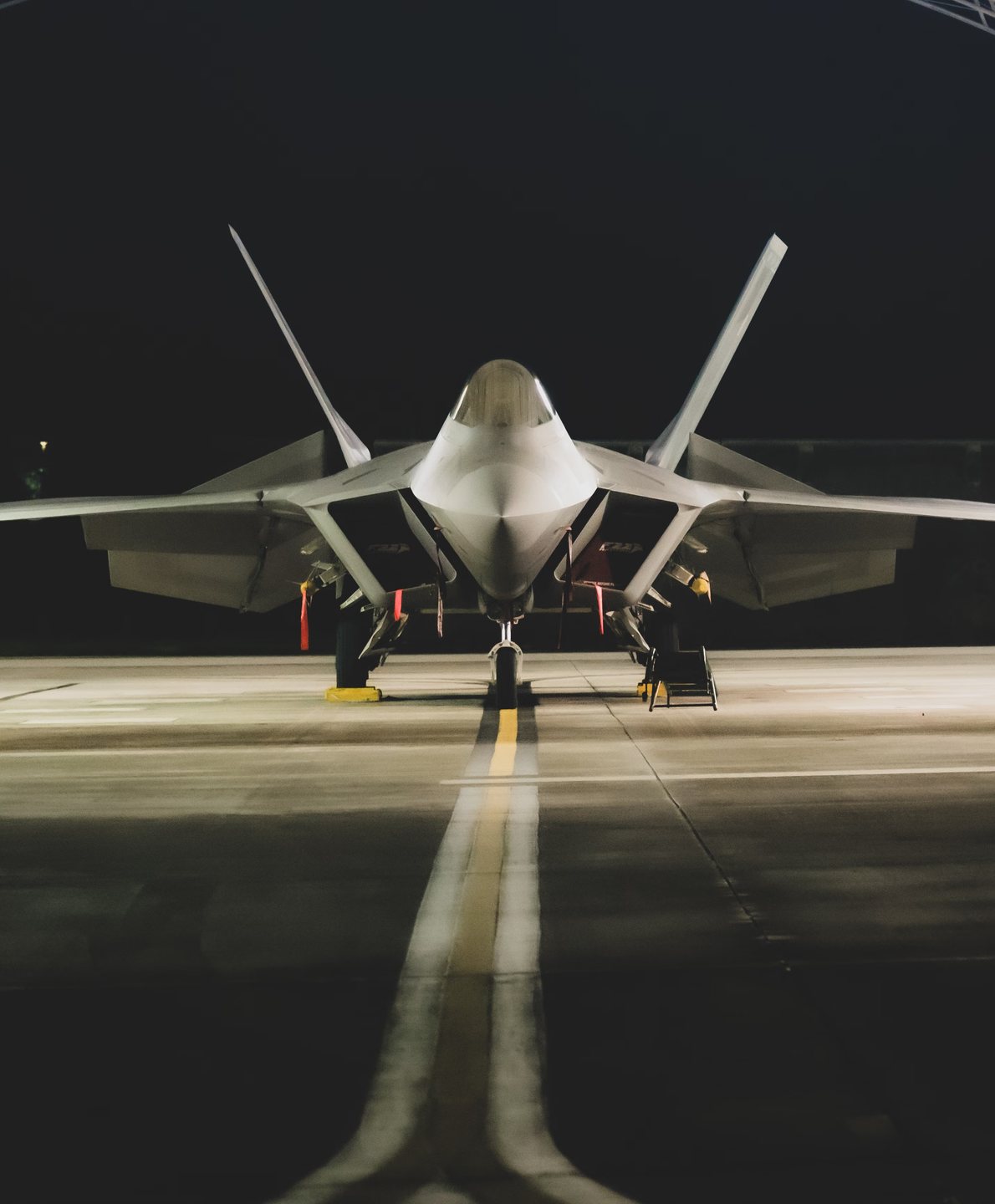 Front view of an angular stealth fighter parked symmetrically on a dark tarmac at night