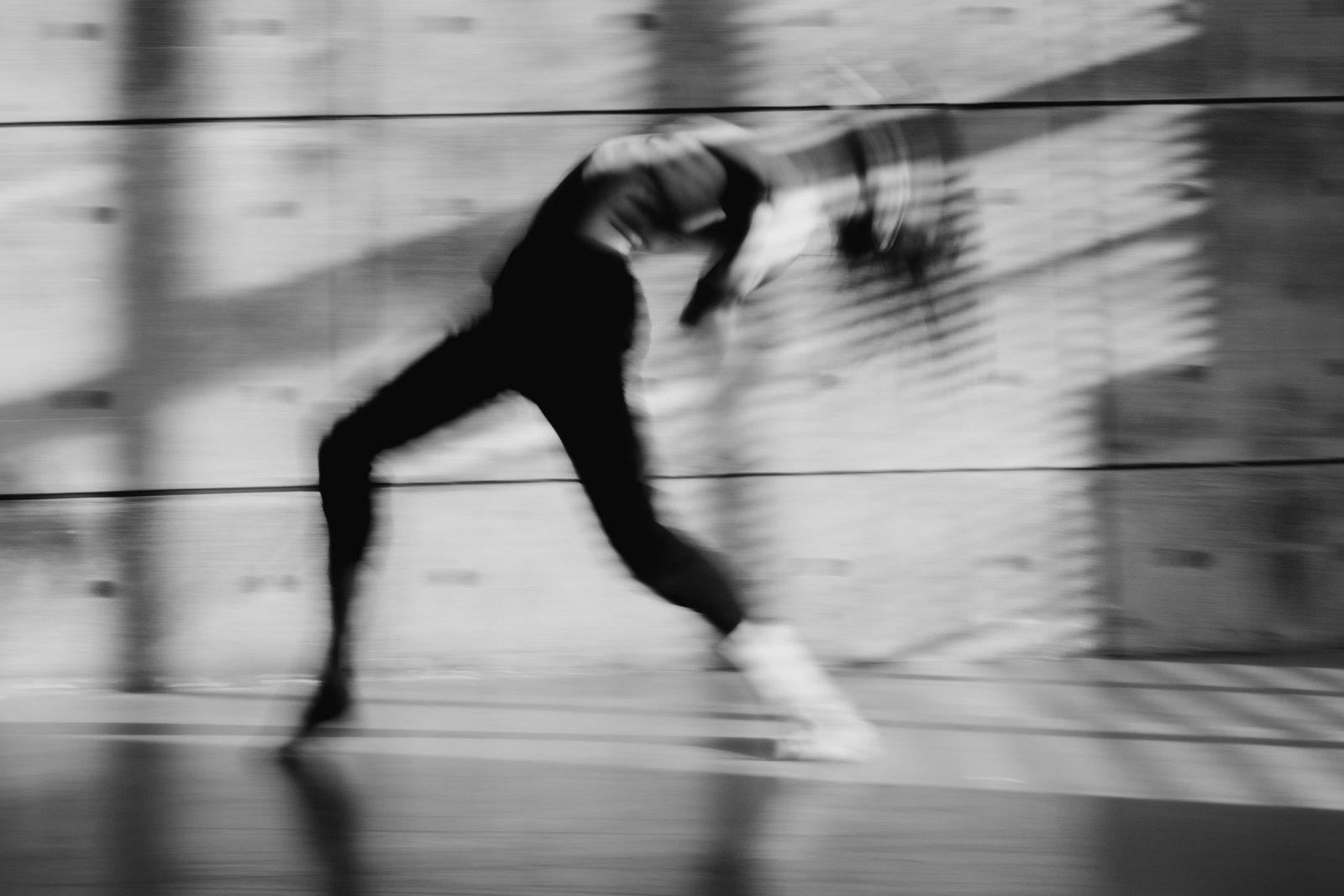 Dancer mid-lunge across shafts of light on a concrete wall