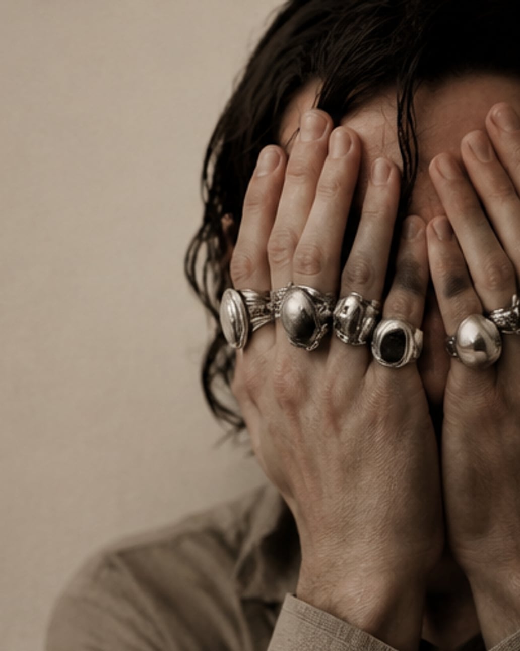 Hands stacked with silver rings covering a face