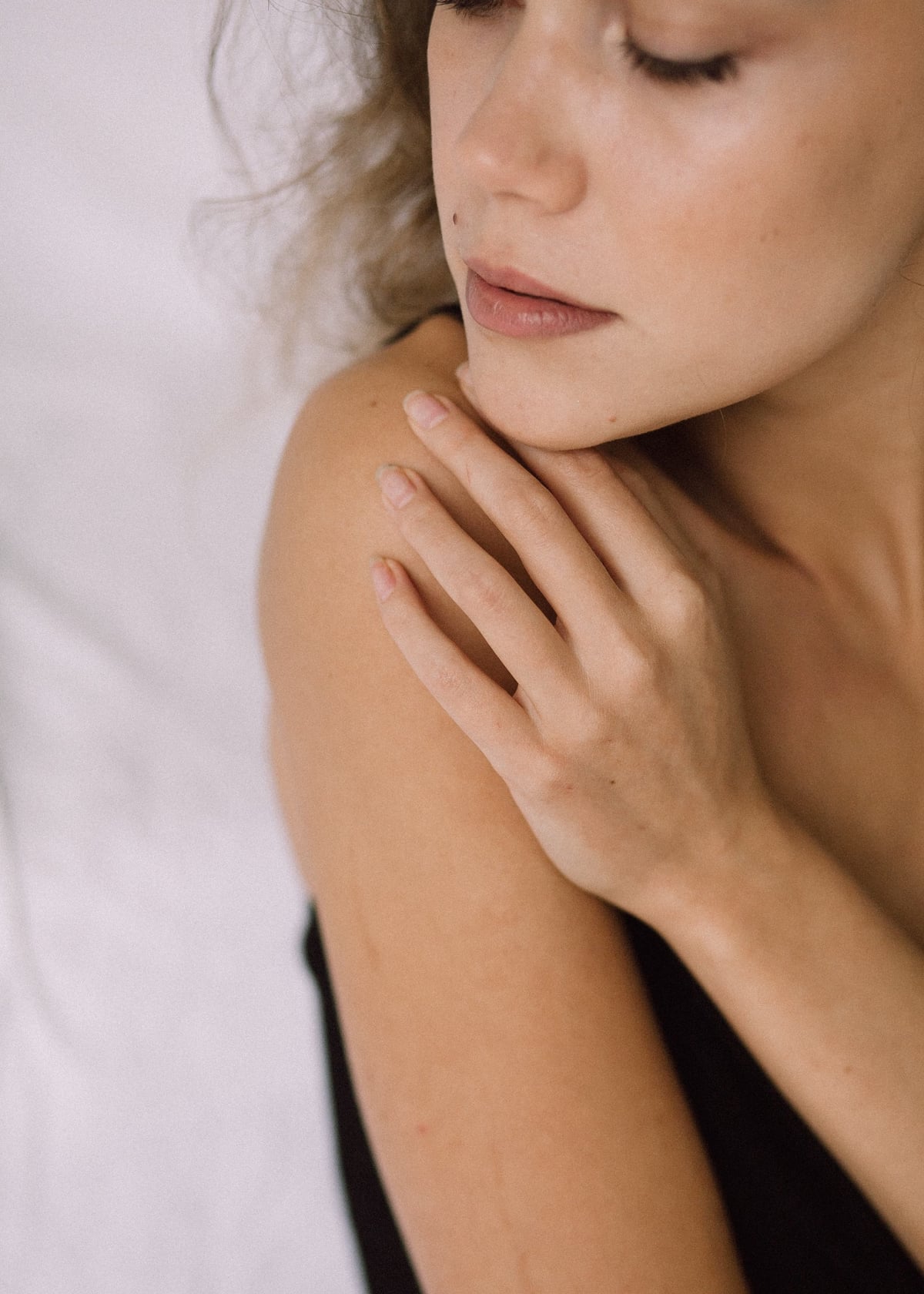A hand resting on a bare shoulder, eyes lowered