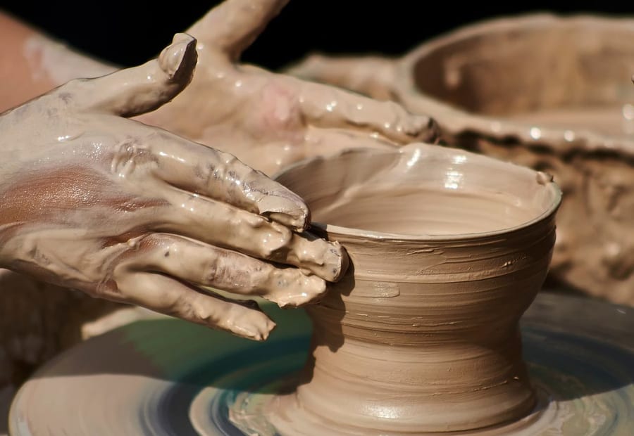 Two hands centring a wet clay bowl on a wheel.