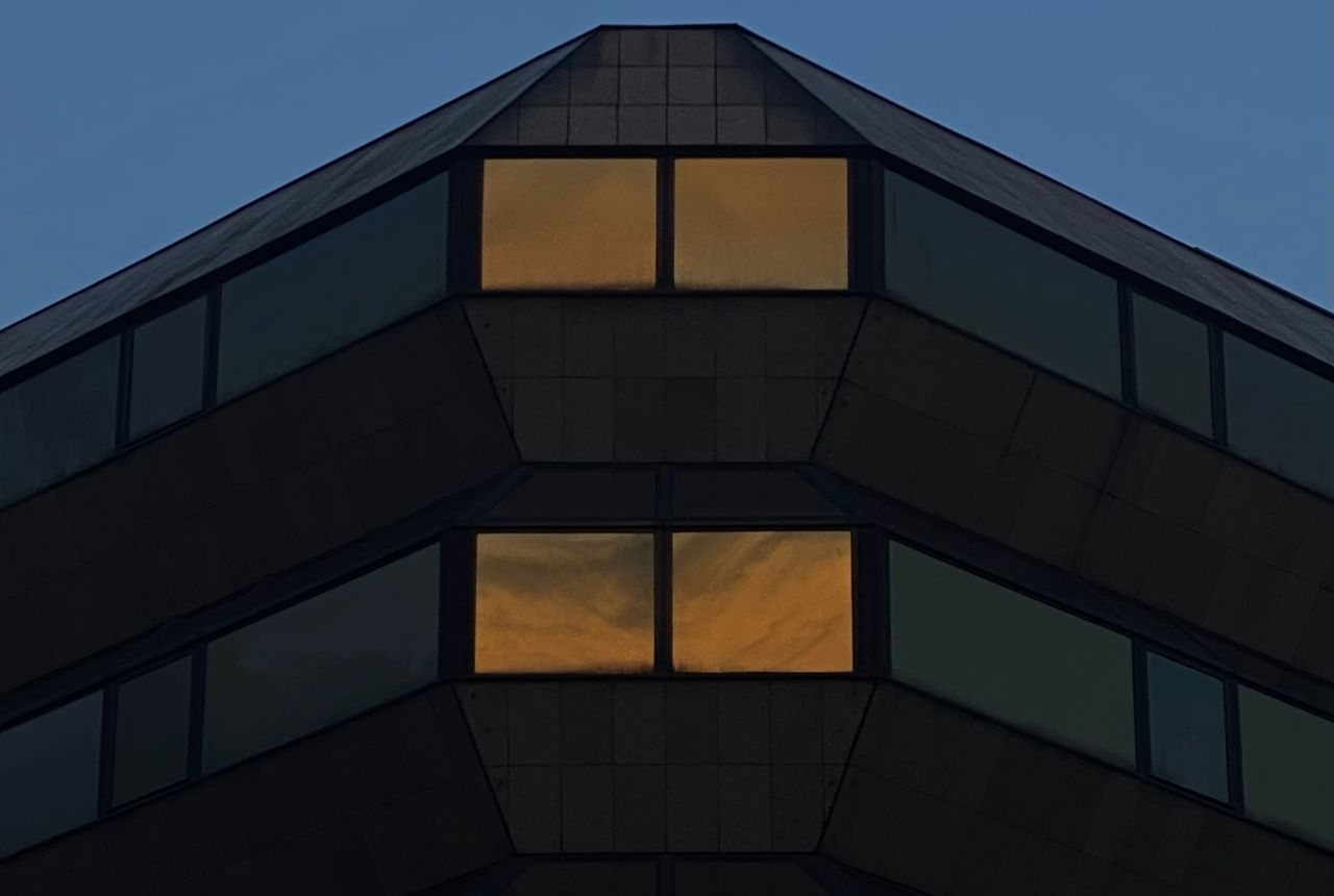 Amber-lit windows glowing on a dark building against a deep blue twilight sky