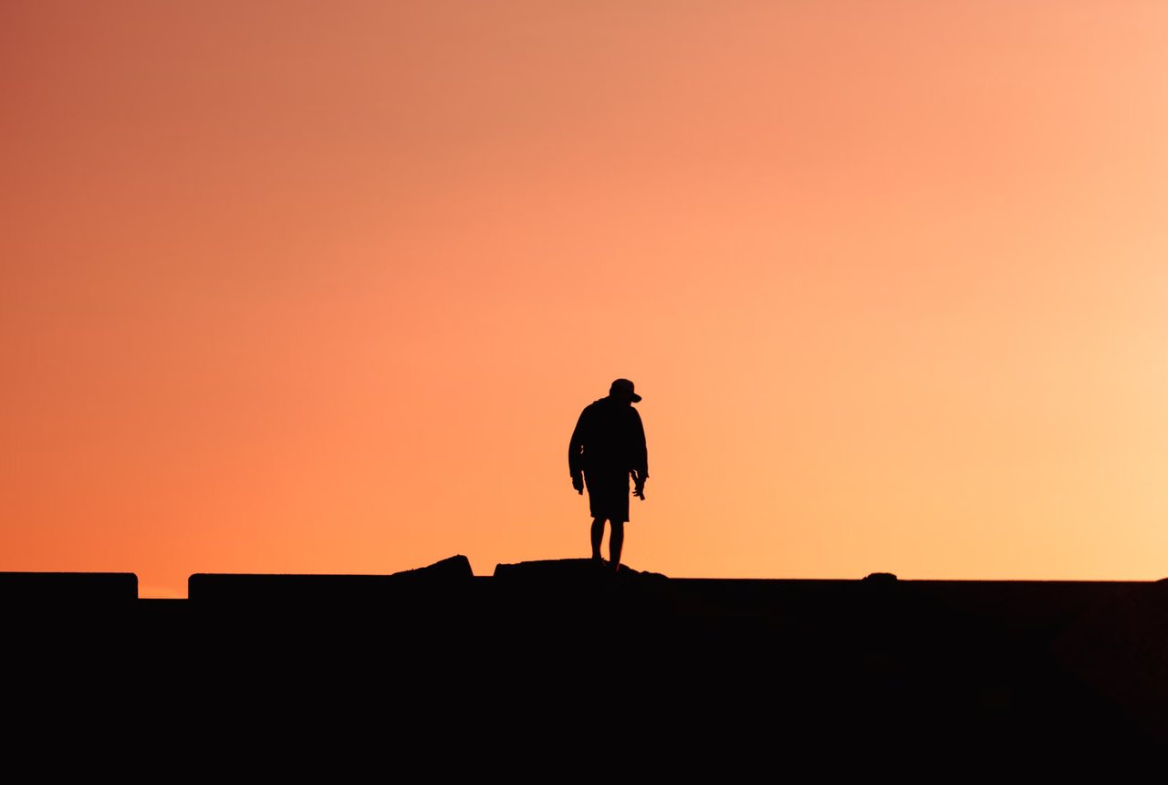 Figure standing on a jetty against the last orange light