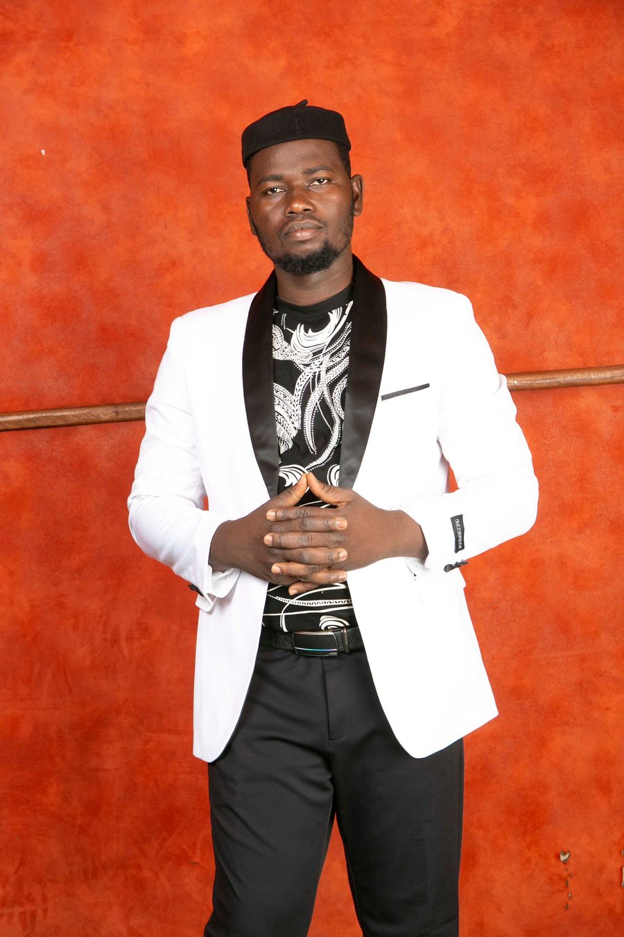 Man in a white tuxedo jacket standing before an oxidised rust-orange wall