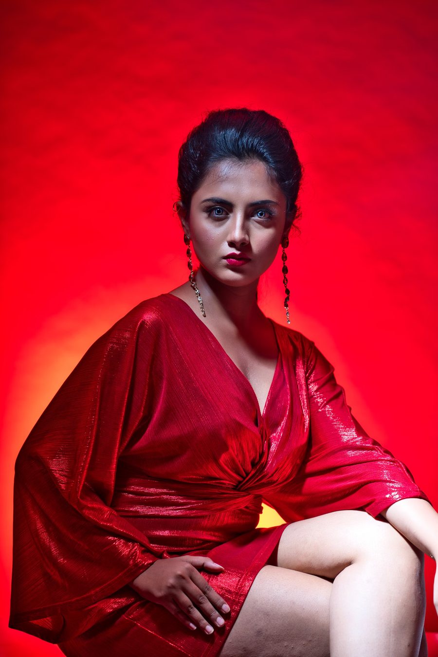 Woman in a red silk dress seated against a red-lit seamless backdrop