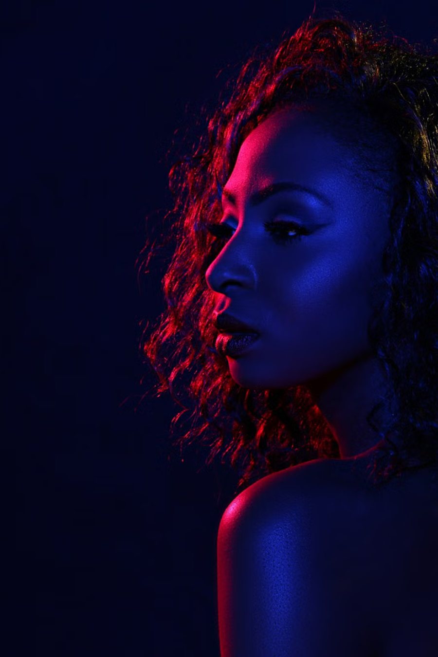 Profile portrait lit only by blue and red gels against near darkness