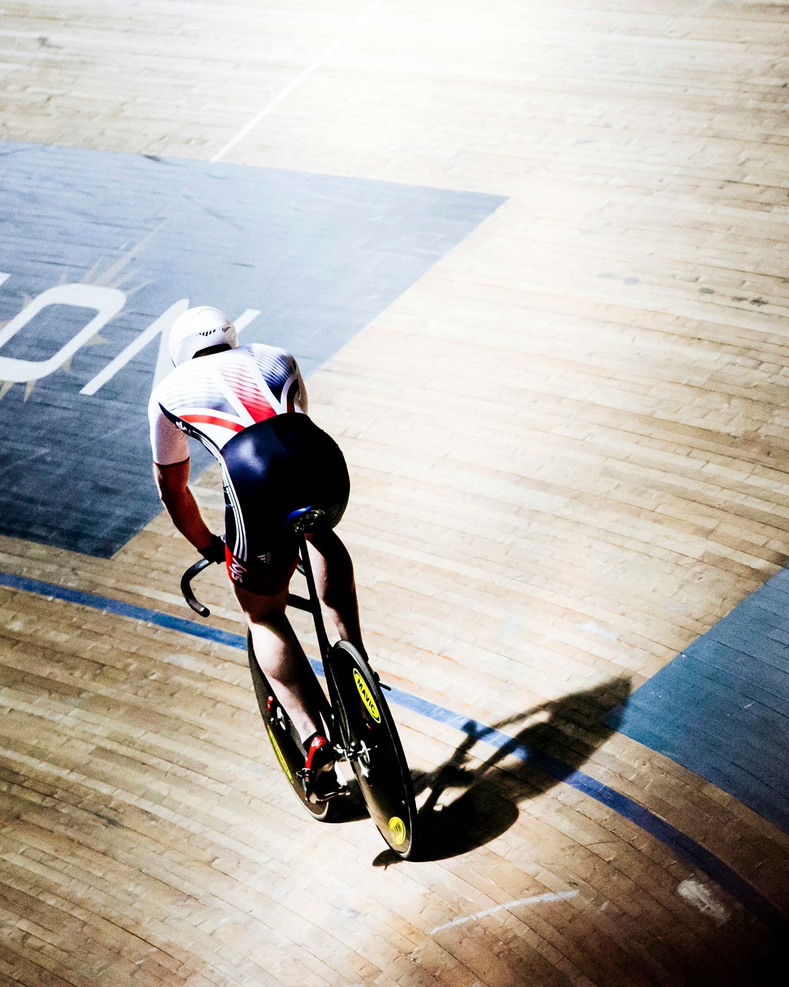 Track cyclist seen from above, riding the pine boards of an indoor velodrome