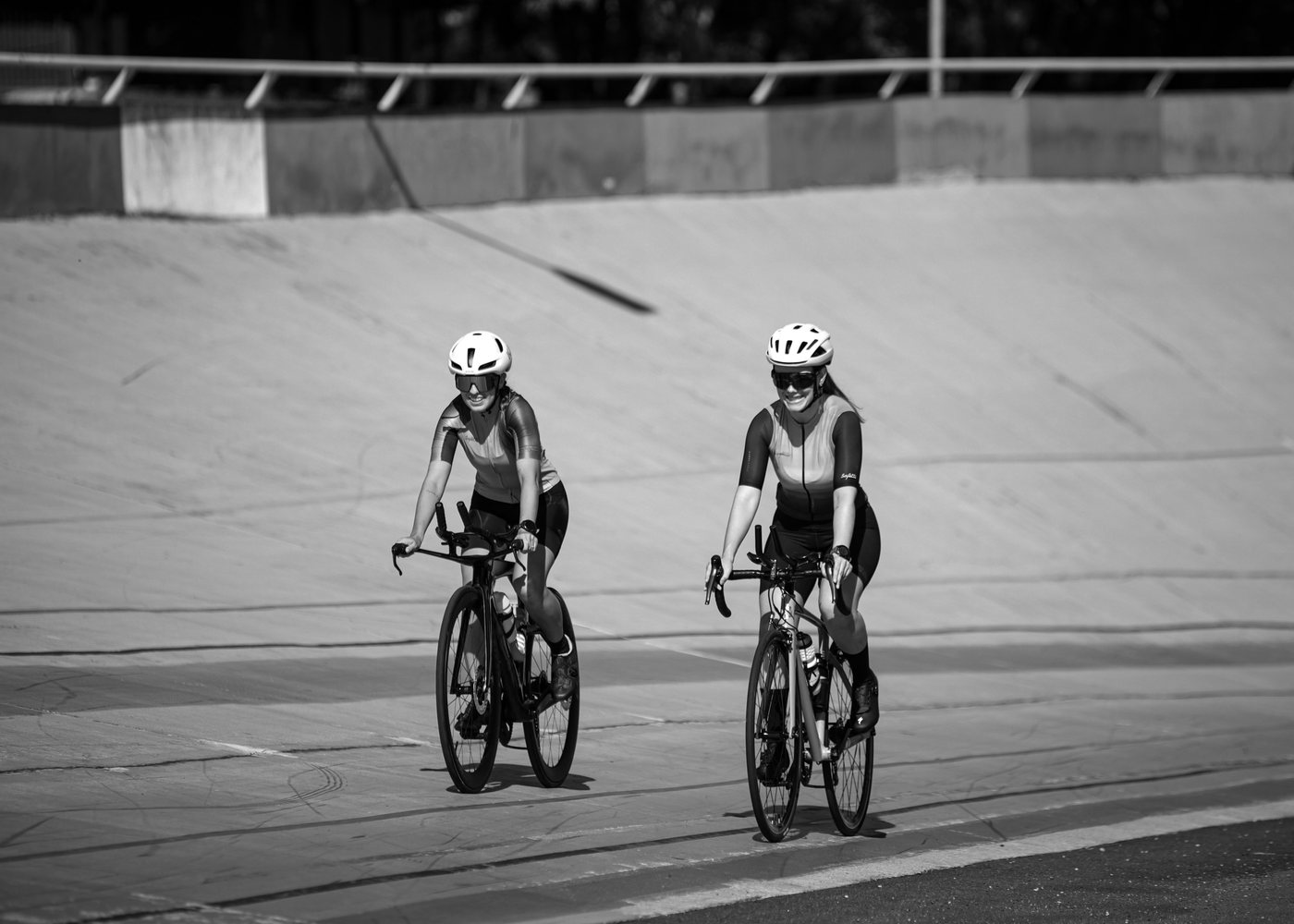 Two riders rolling side by side on the banking of an outdoor velodrome