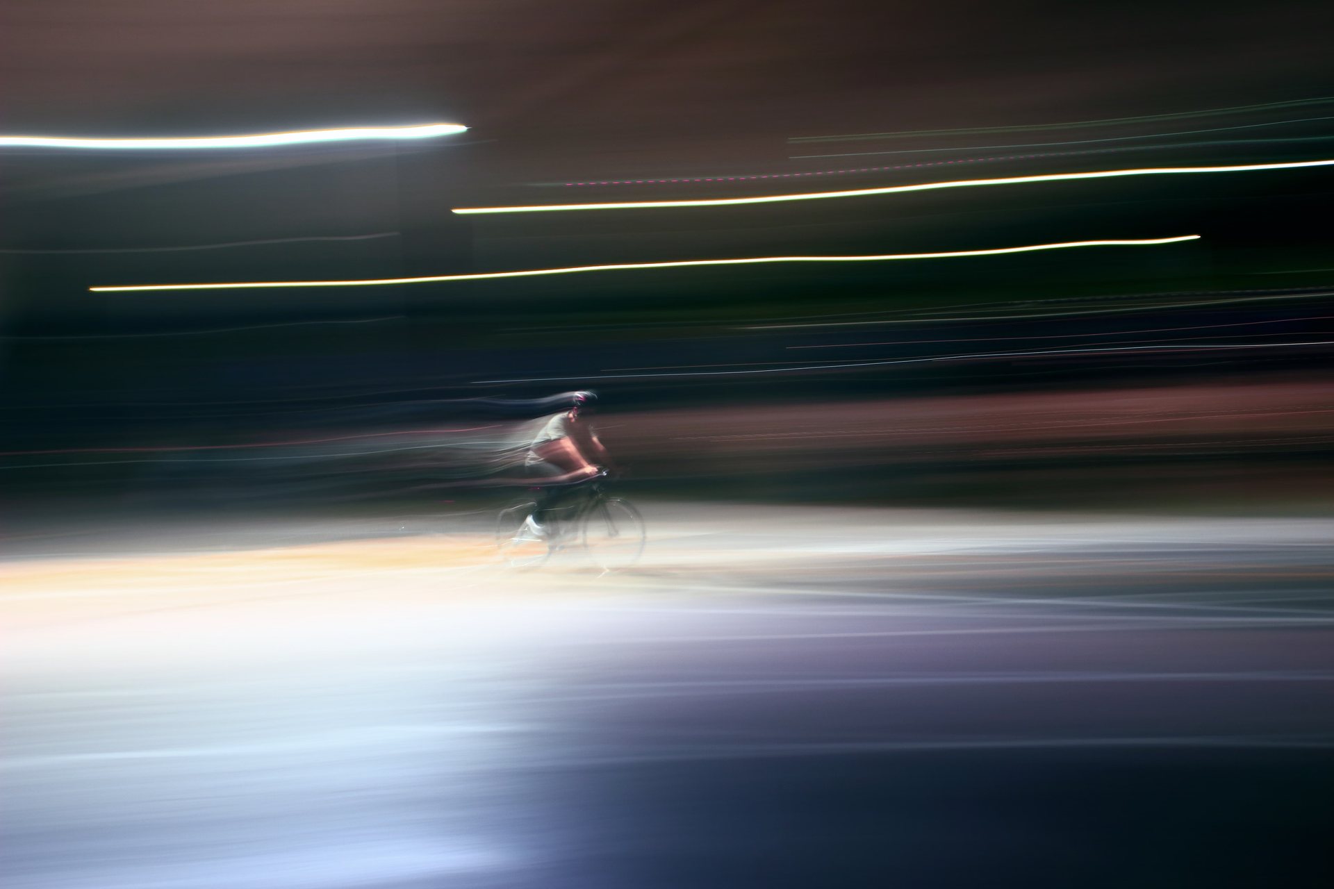 Cyclist streaking through the night, light trails smeared by a slow shutter