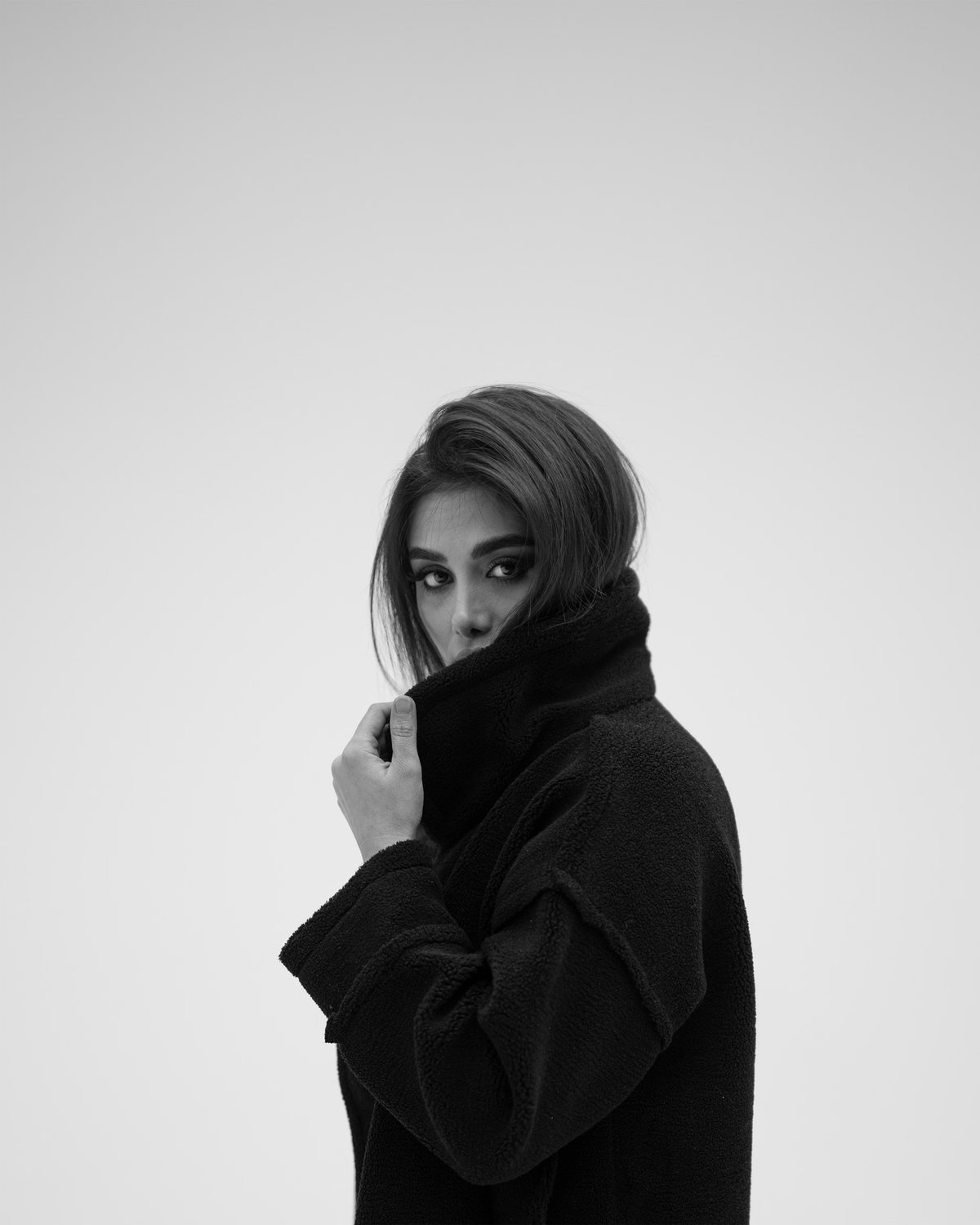 Woman holding the collar of a black felted-wool coat against a white studio wall