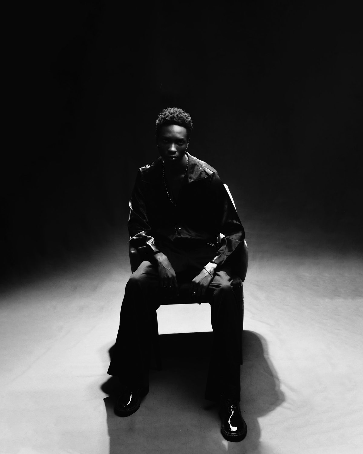 Man seated on a stool in a dark studio, dressed in black