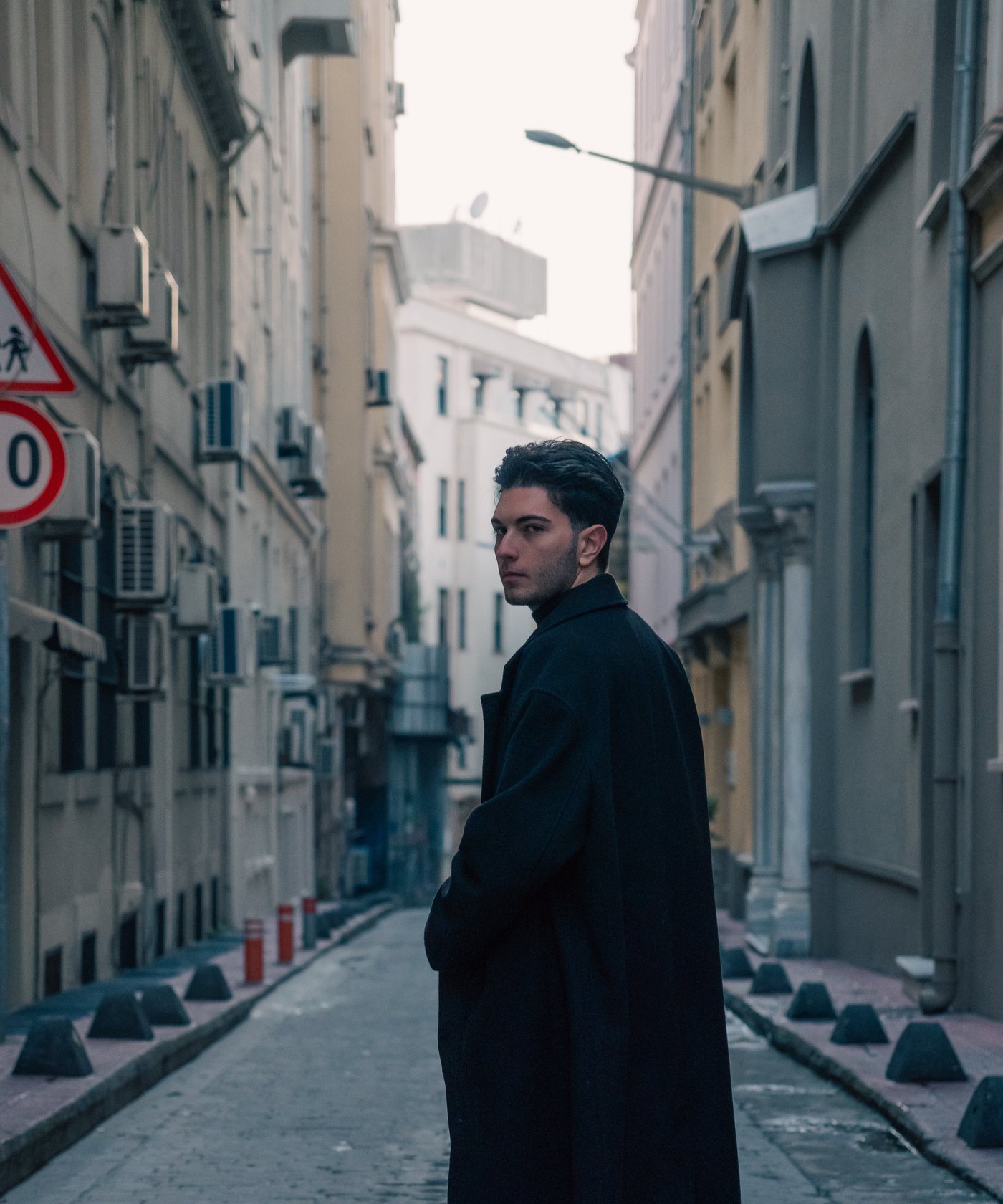 Man glancing back over the shoulder of a slate overcoat in a narrow grey street