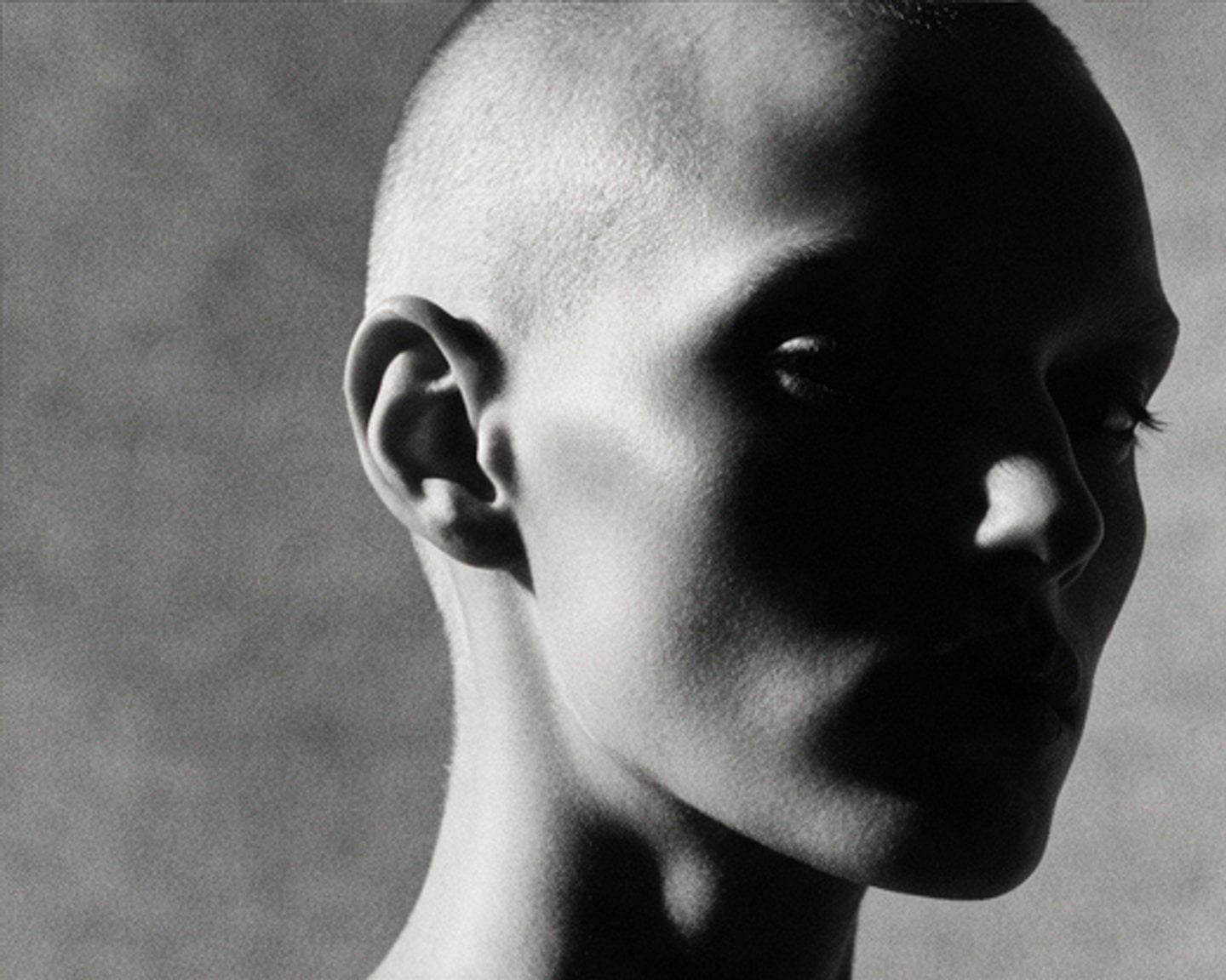 Black and white studio portrait with a shaved head, lit from one side