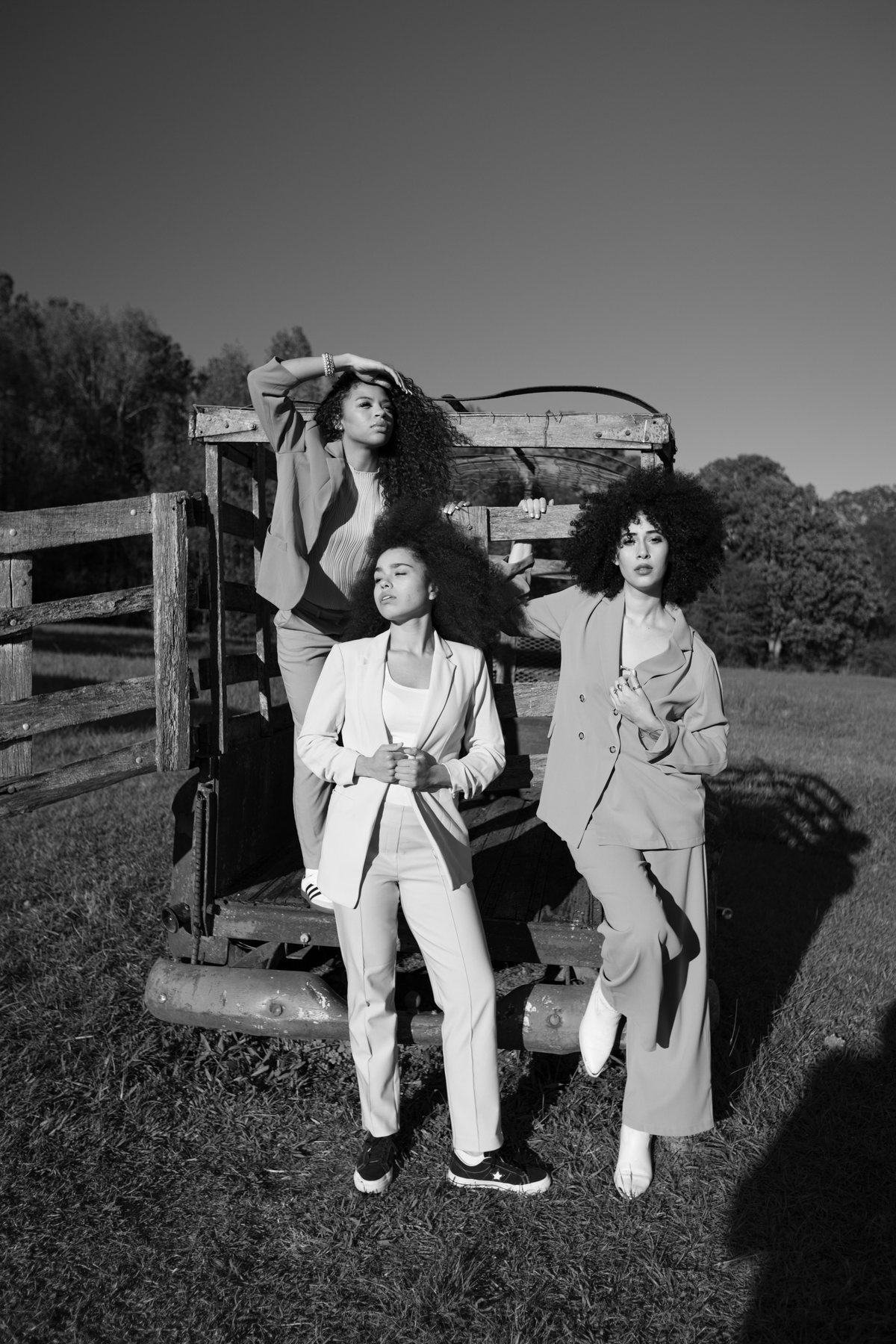 Three women in relaxed suits by a wooden cart, black and white, last light