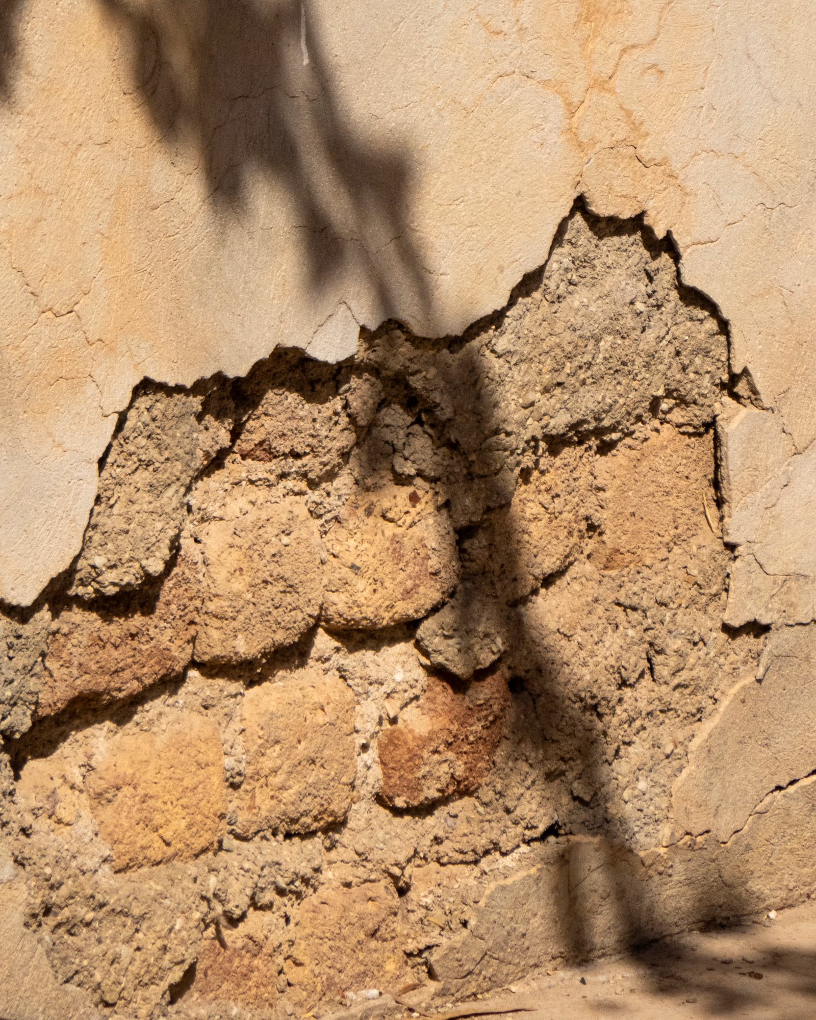 A weathered lime-plaster wall cracking to reveal the earthen substrate beneath