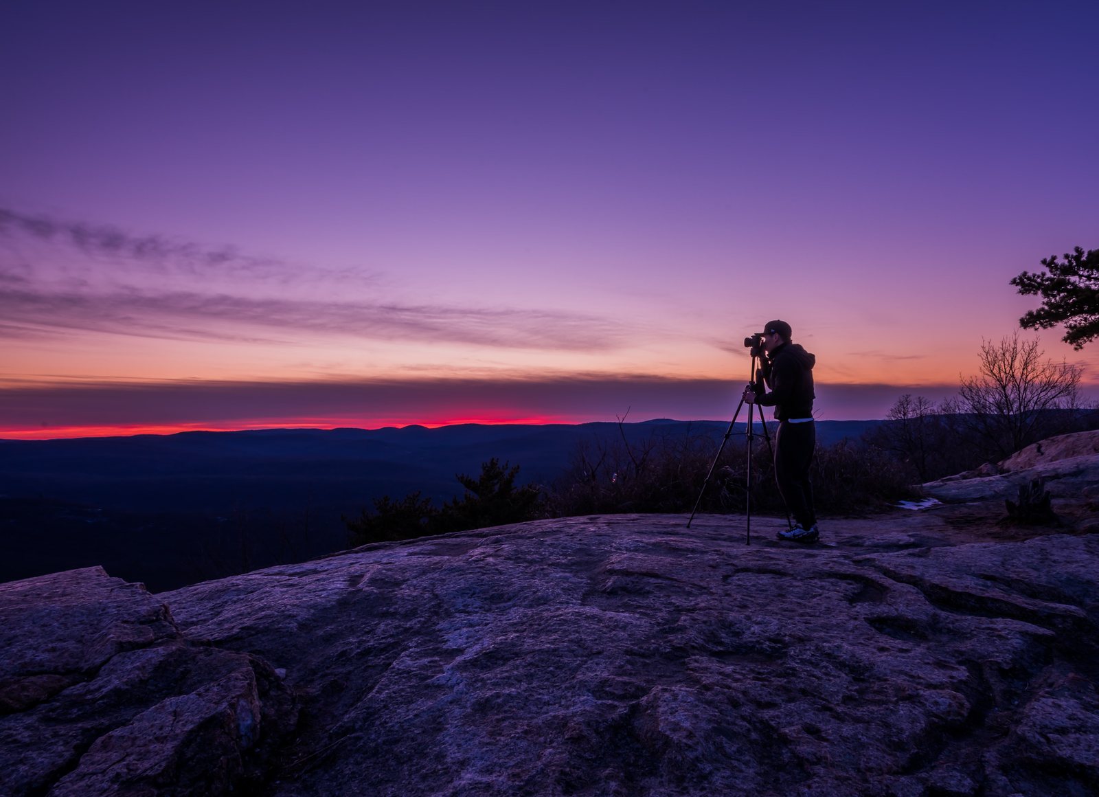 Photographer at a tripod on a rock ledge at blue hour