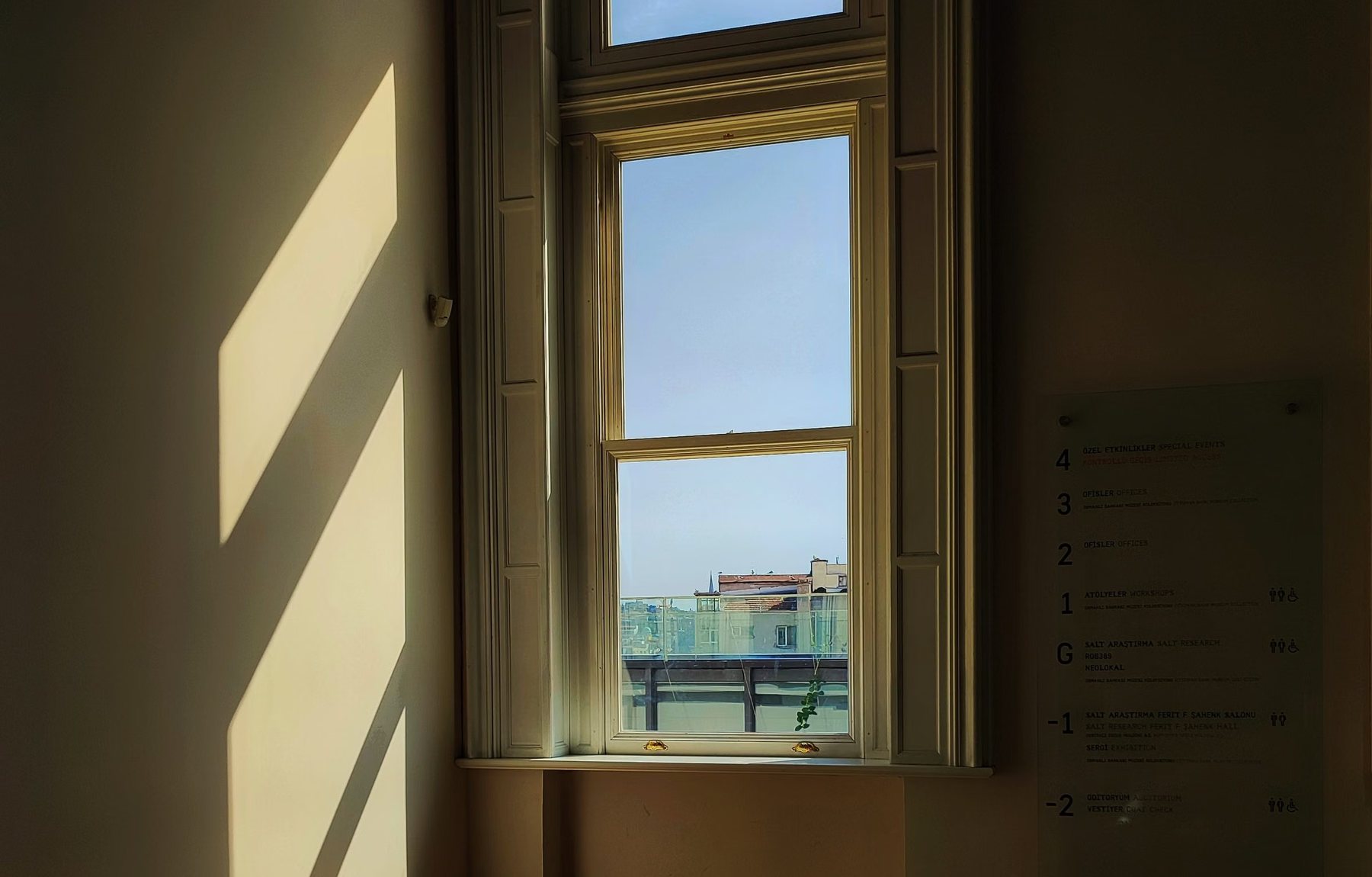 Sunlight cutting hard diagonals across a plastered gallery room