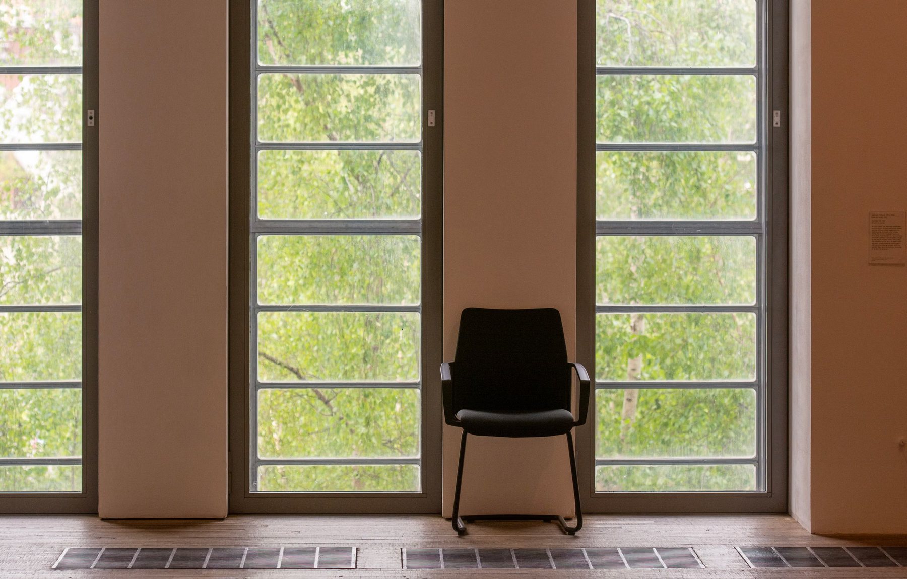 A single chair set against tall windows looking into green