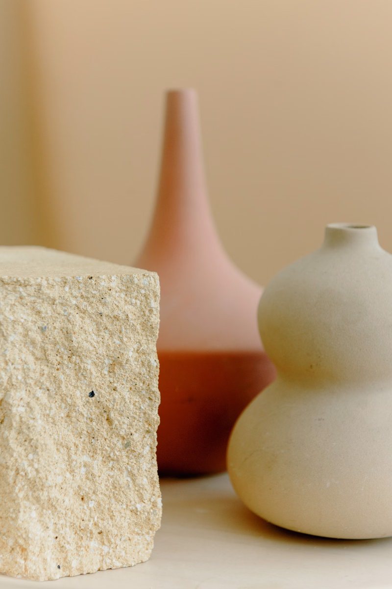 Blush and cream glazed vessels beside a rough stone cube