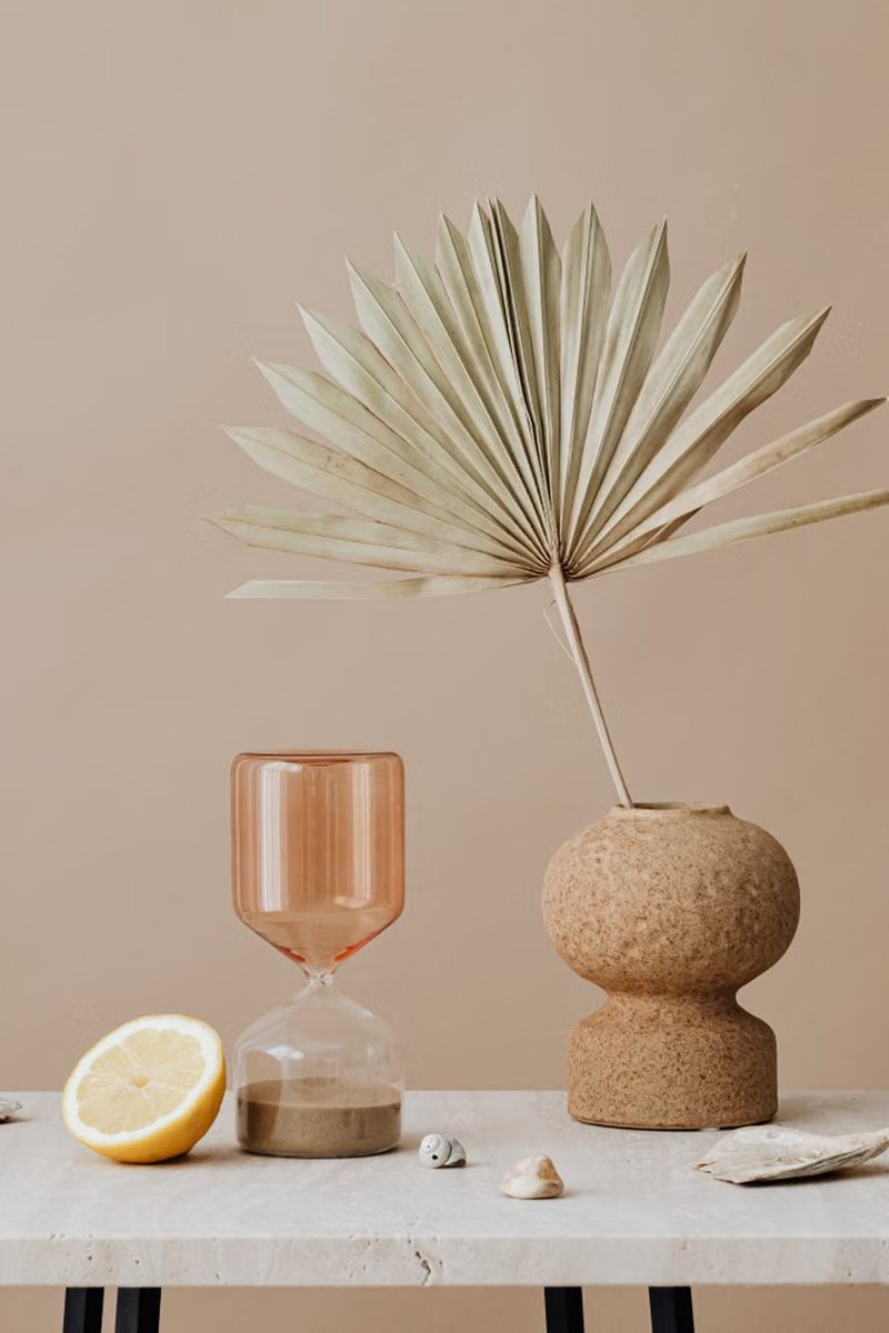 Still life of a sand-glazed vessel, fan palm and hourglass