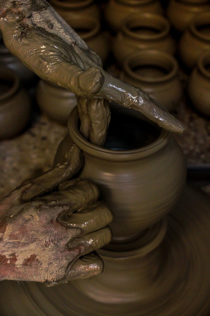 Muddy hands resting on rows of raw earthenware pots