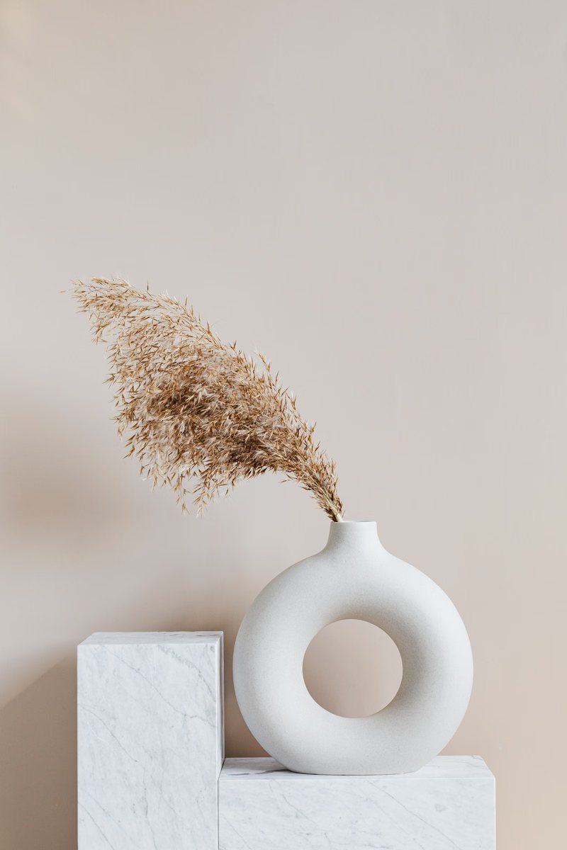White ring-shaped vase with dried grass on stacked plinths