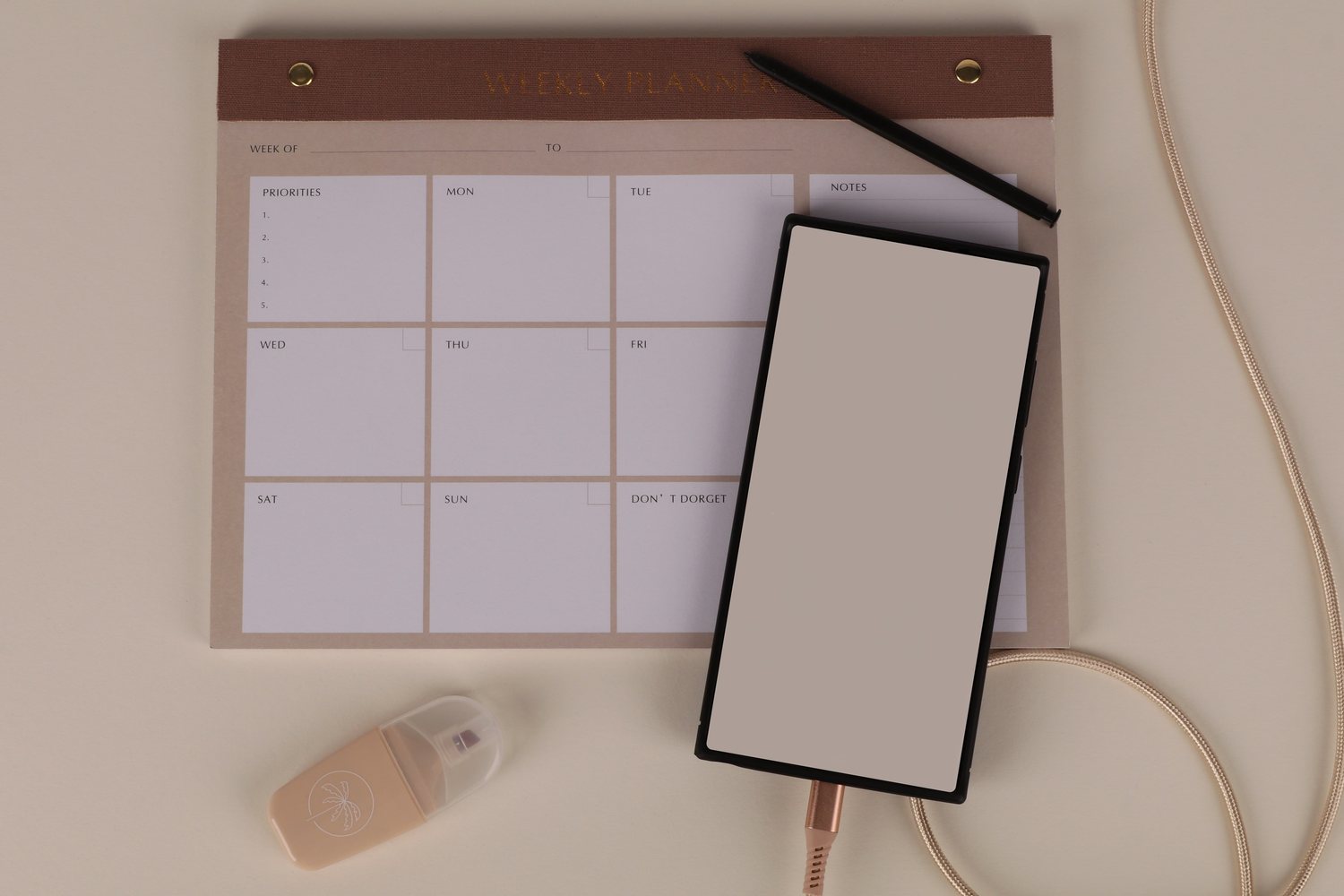 A weekly planner, phone, and pen laid out on a warm neutral surface