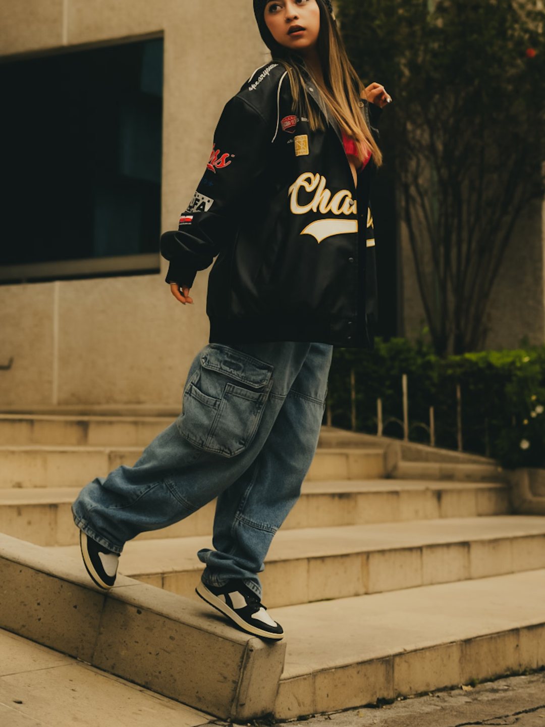 Varsity jacket and washed baggy denim on concrete steps