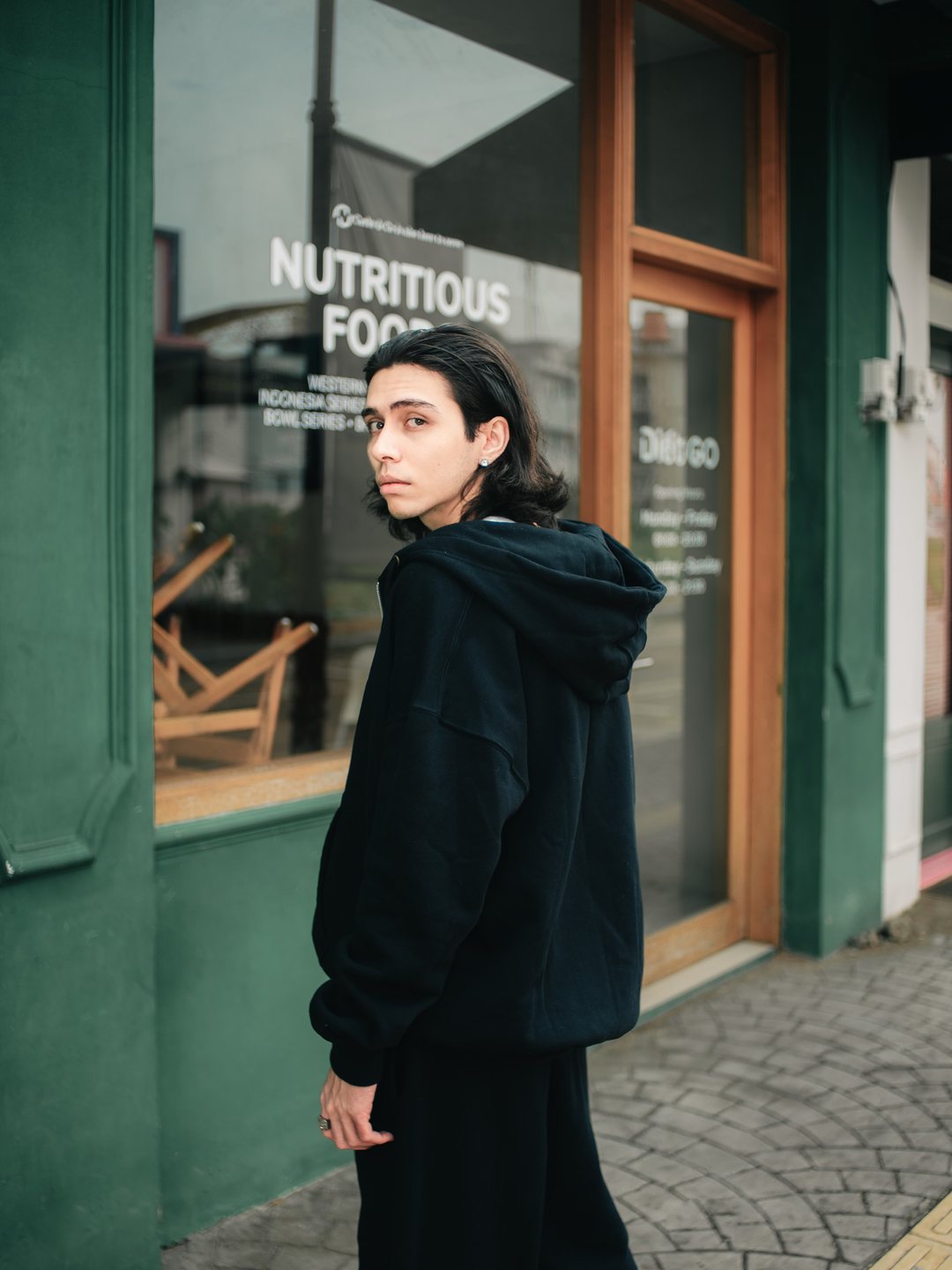 Oversized black hoodie outside a corner storefront