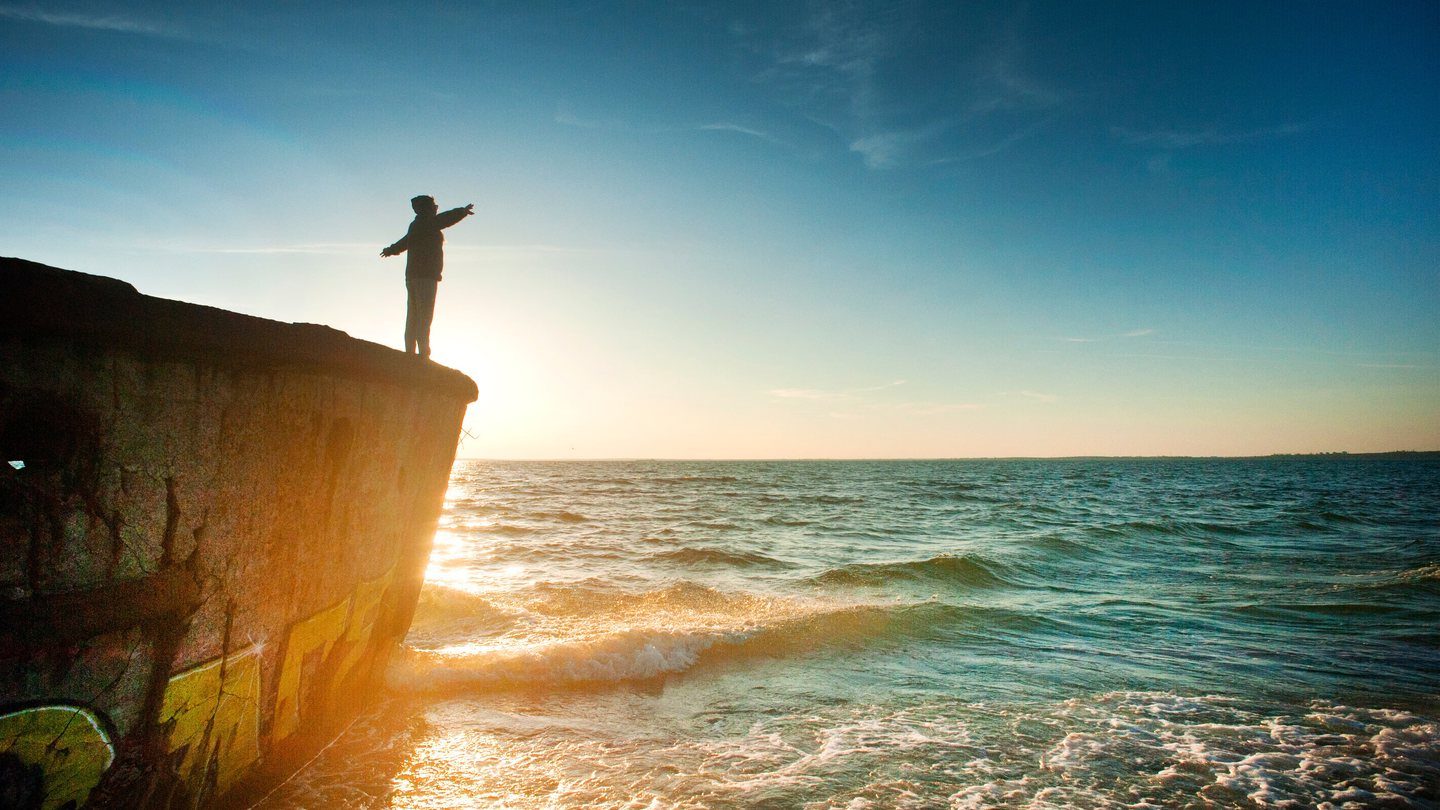 A lone figure on a rock ledge above the sea during golden hour