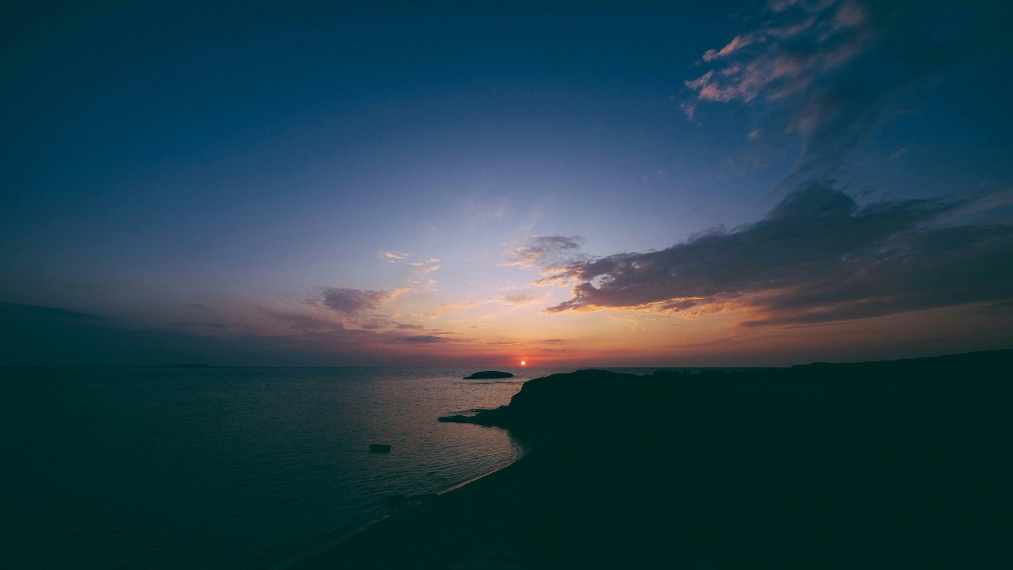 A headland silhouetted against the sea as the sun drops to dusk