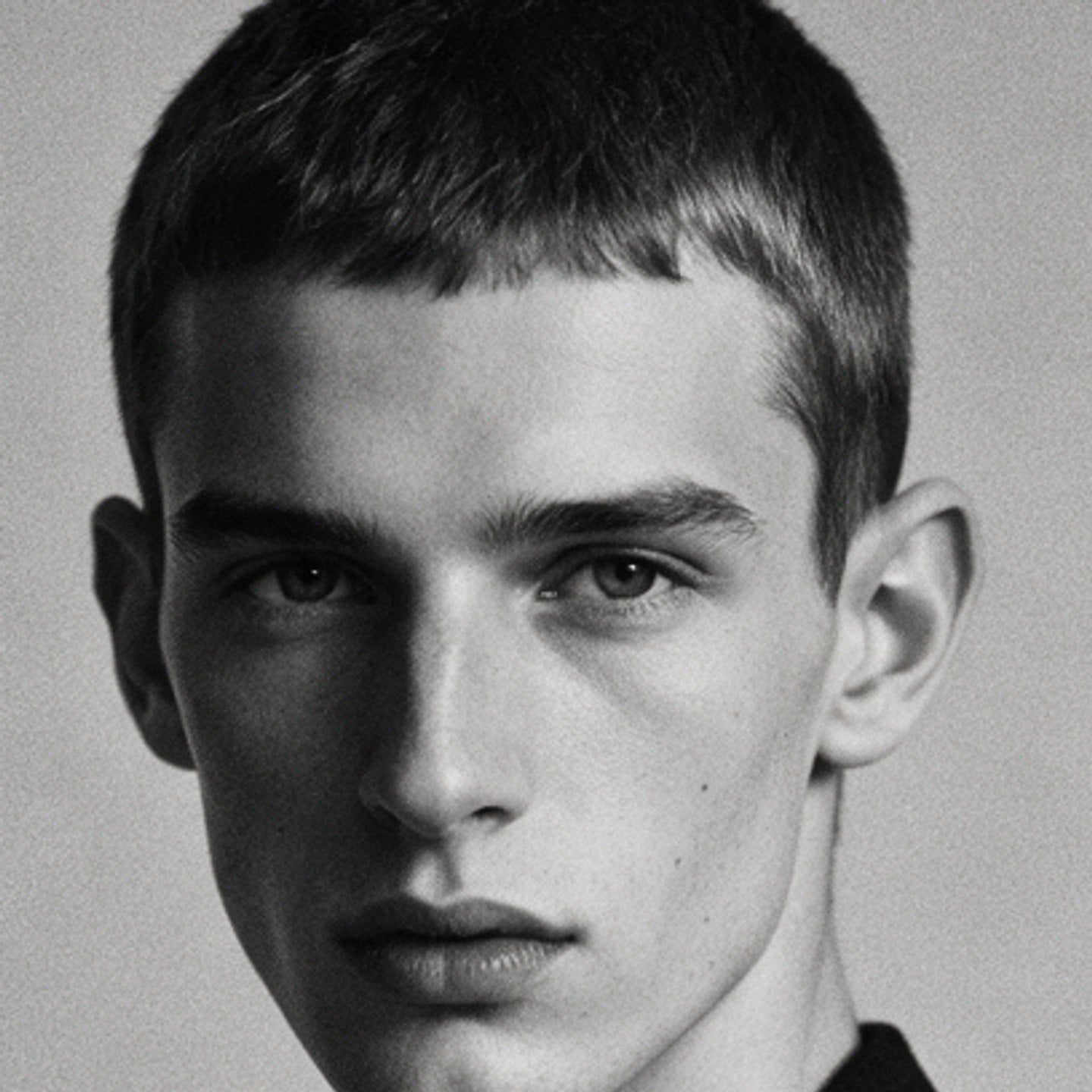 Black-and-white portrait of a young man with cropped hair looking into the lens