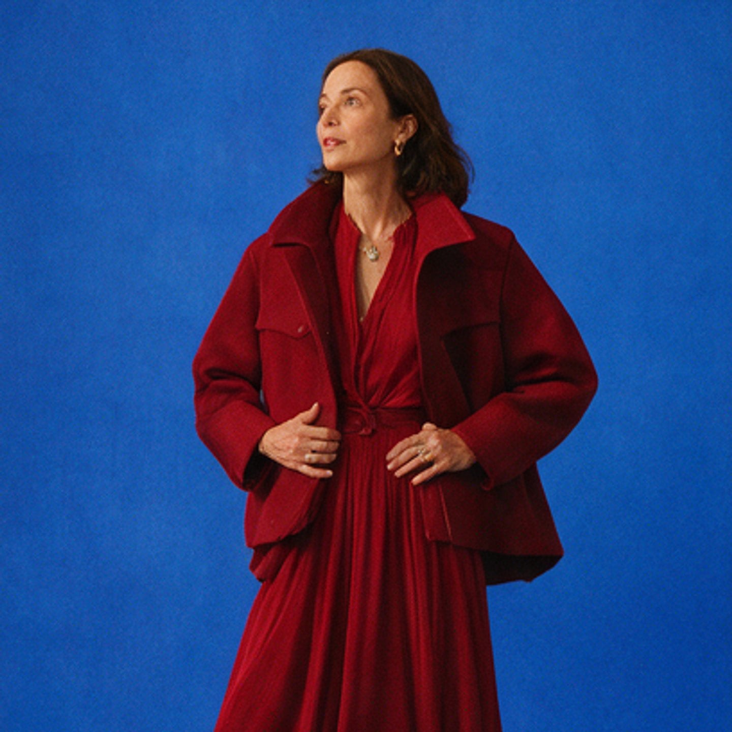 Woman in a crimson coat and dress against a cobalt blue studio backdrop