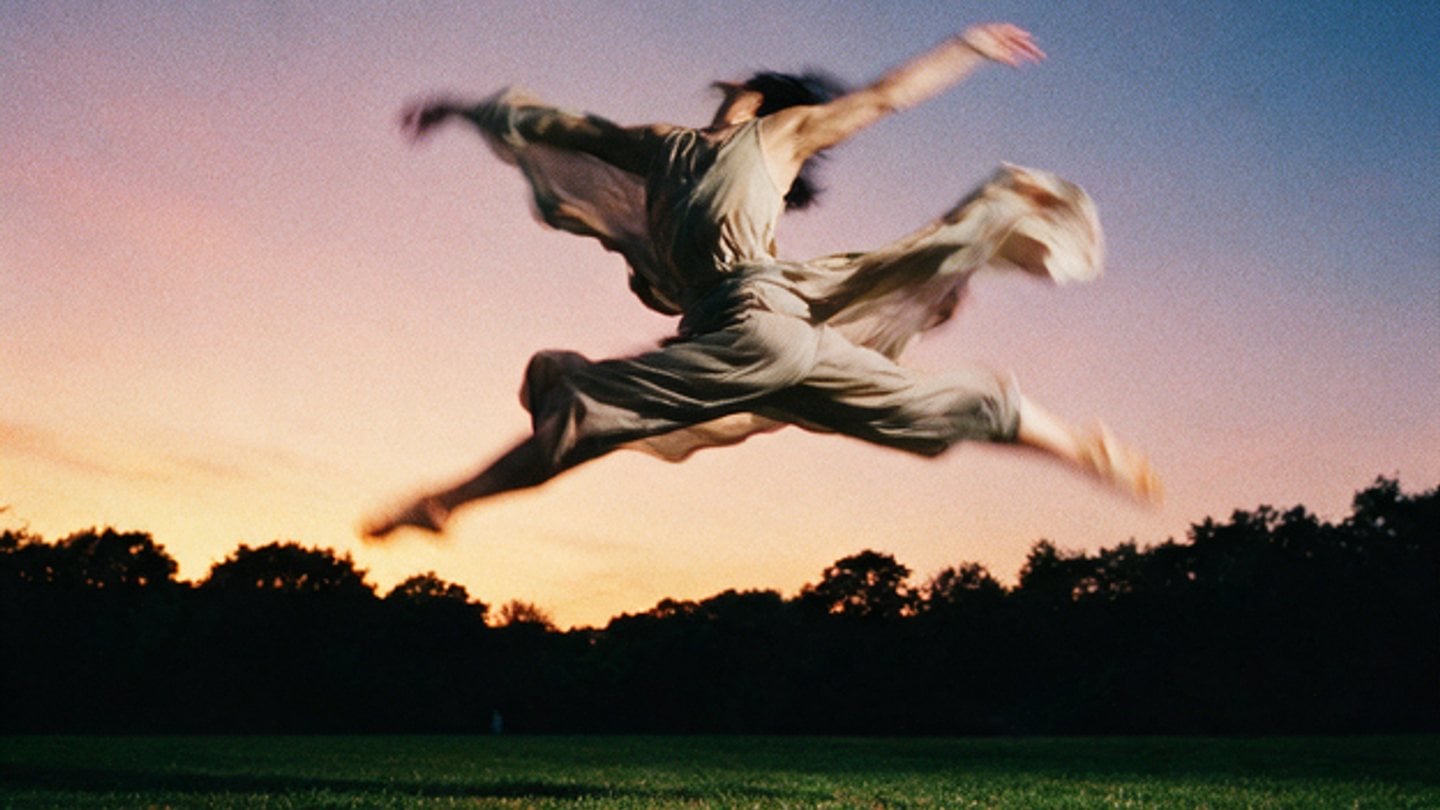 A dancer suspended mid-leap over a field at dusk